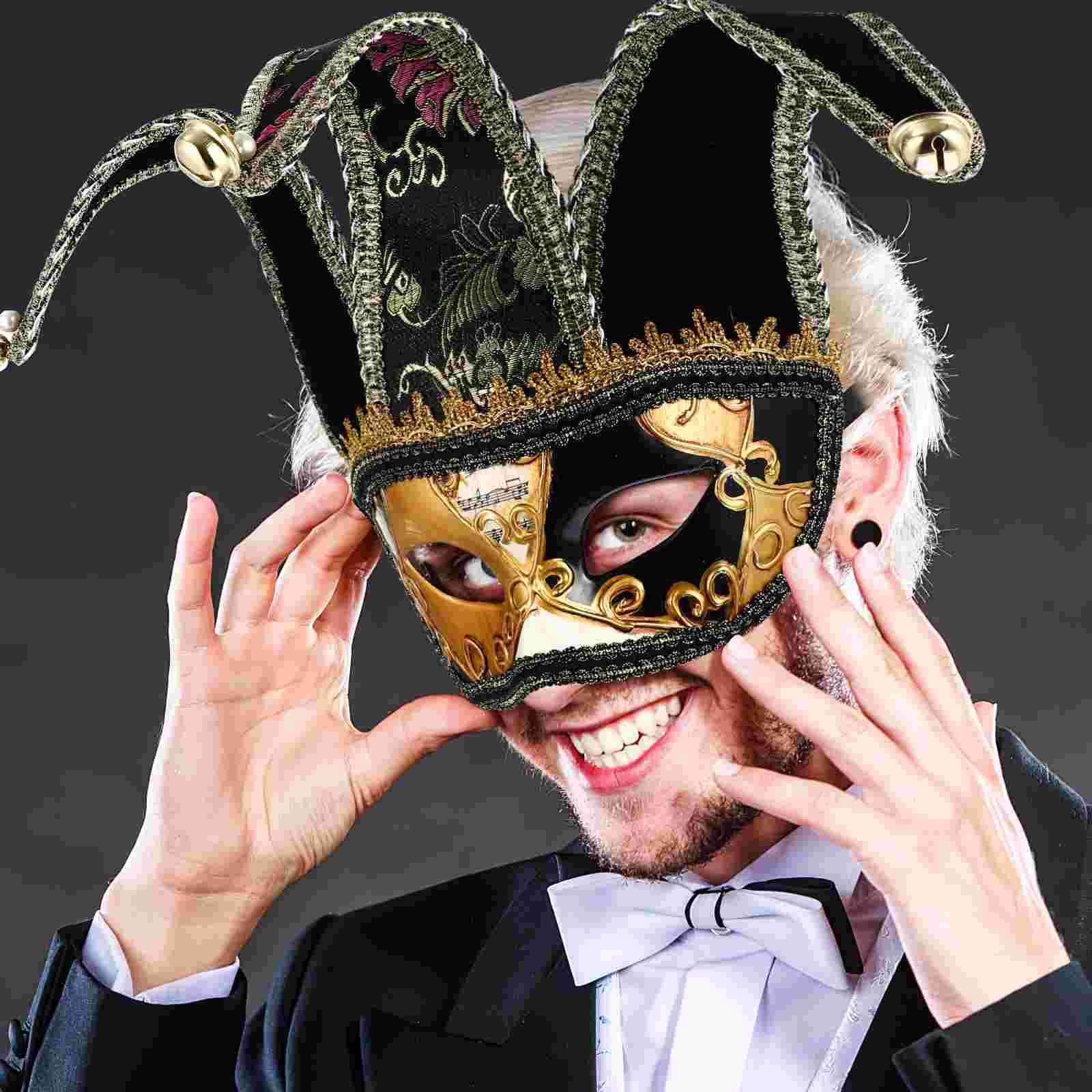 Masque vénitien demi Joker noir et doré avec motifs baroques et clochettes porté de face avec mains ajustant le masque