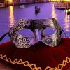 Masque carnaval de Venise argent antique avec motifs baroques en relief sur fond argenté, posé sur coussin rouge