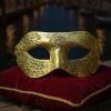 Masque Carnaval de Venise doré antique en métal avec motifs gravés, posé sur un coussin rouge velours