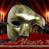 Masque Carnaval De Venise doré demi-visage en métal avec finition texturée, présenté sur tissu rouge brodé avec chandeliers allumés en arrière-plan
