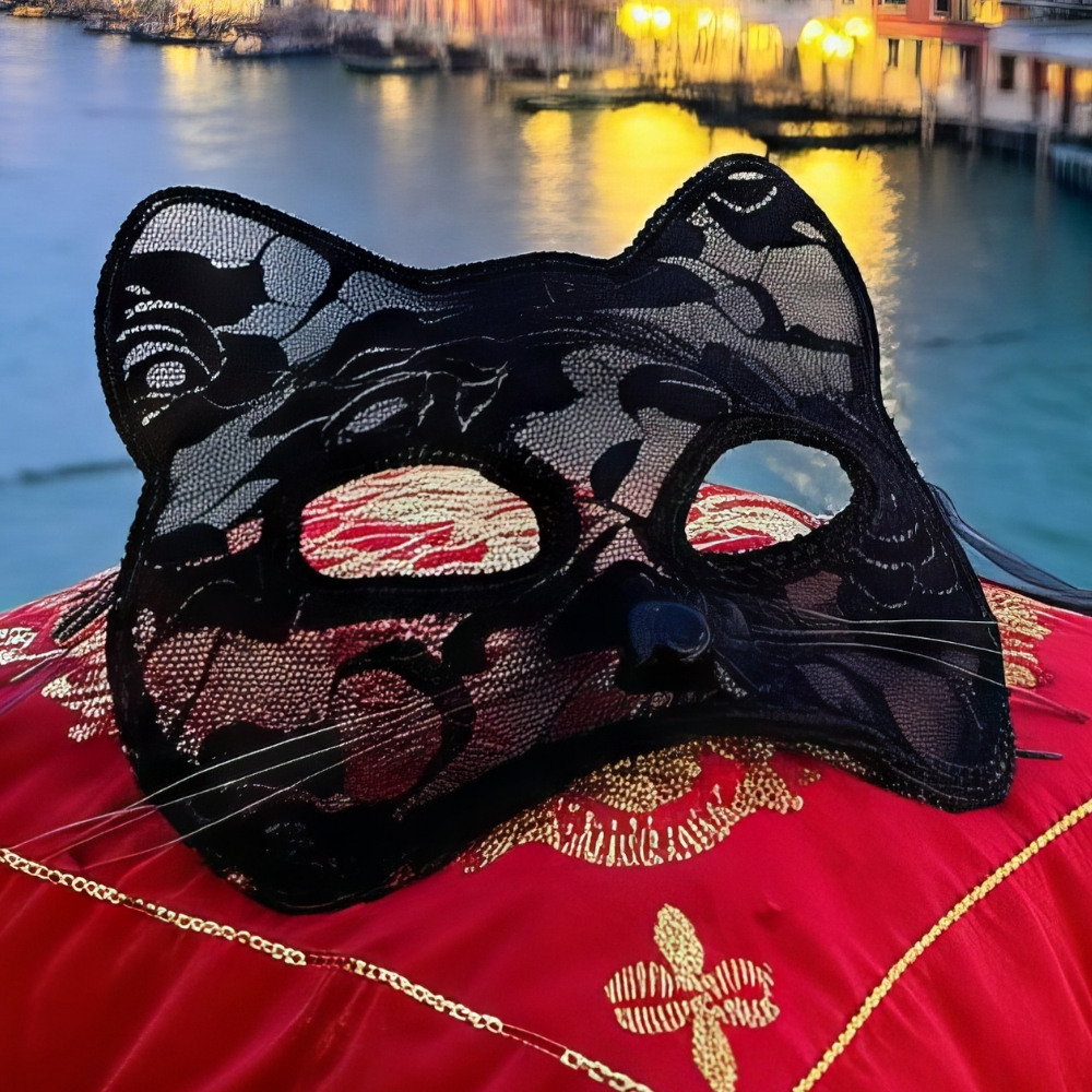 Masque chat vénitien en dentelle noire avec motif floral délicat posé sur un coussin rouge brodé, décor élégant pour fête masquée
