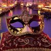 Masque Commedia Dell’Arte musical rouge noir et or avec décorations dorées et motif de partition musicale, posé sur coussin rouge brodé, fond canal vénitien au crépuscule