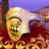 Masque demi-visage Arlequin argent et noir avec motif losanges et décor baroque posé sur tissu rouge brodé doré