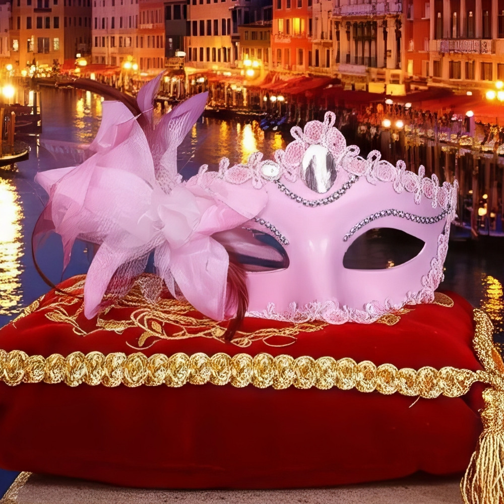Masque vénitien rose en matière rigide avec décorations en strass et dentelle, orné de plumes roses, posé sur un coussin rouge brodé doré, fond de canal vénitien illuminé
